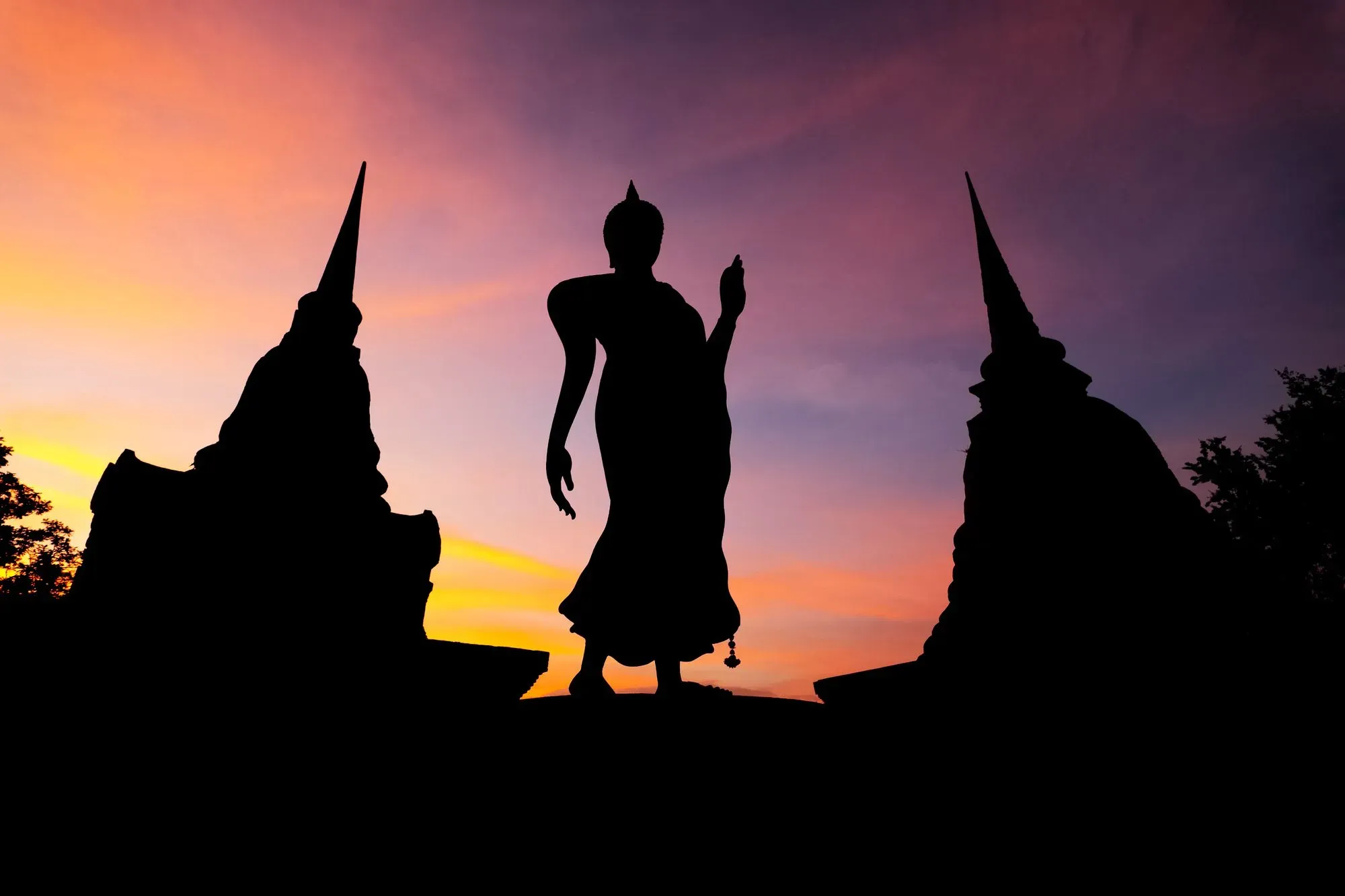 L'ombre d'une statue d'un Bouddha  qui marche entourée de deux stupas anciennes dans le parc historique de Sukhothai en Thaïlande.